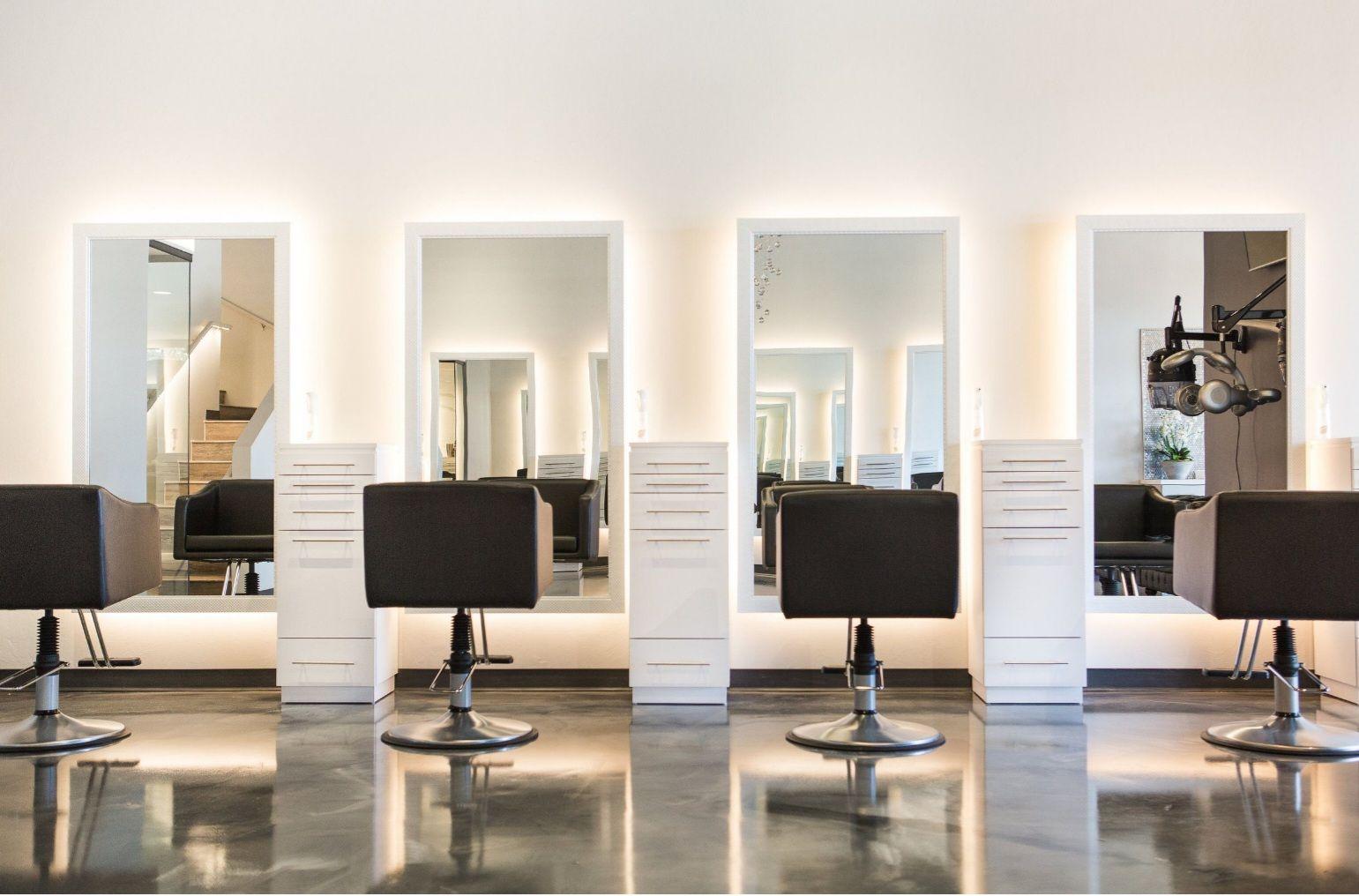 Modern hair salon interior with four styling stations, large mirrors, black chairs, and white cabinets.